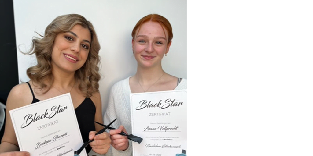 Zwei junge Friseurinnen präsentieren ihre Urkunden